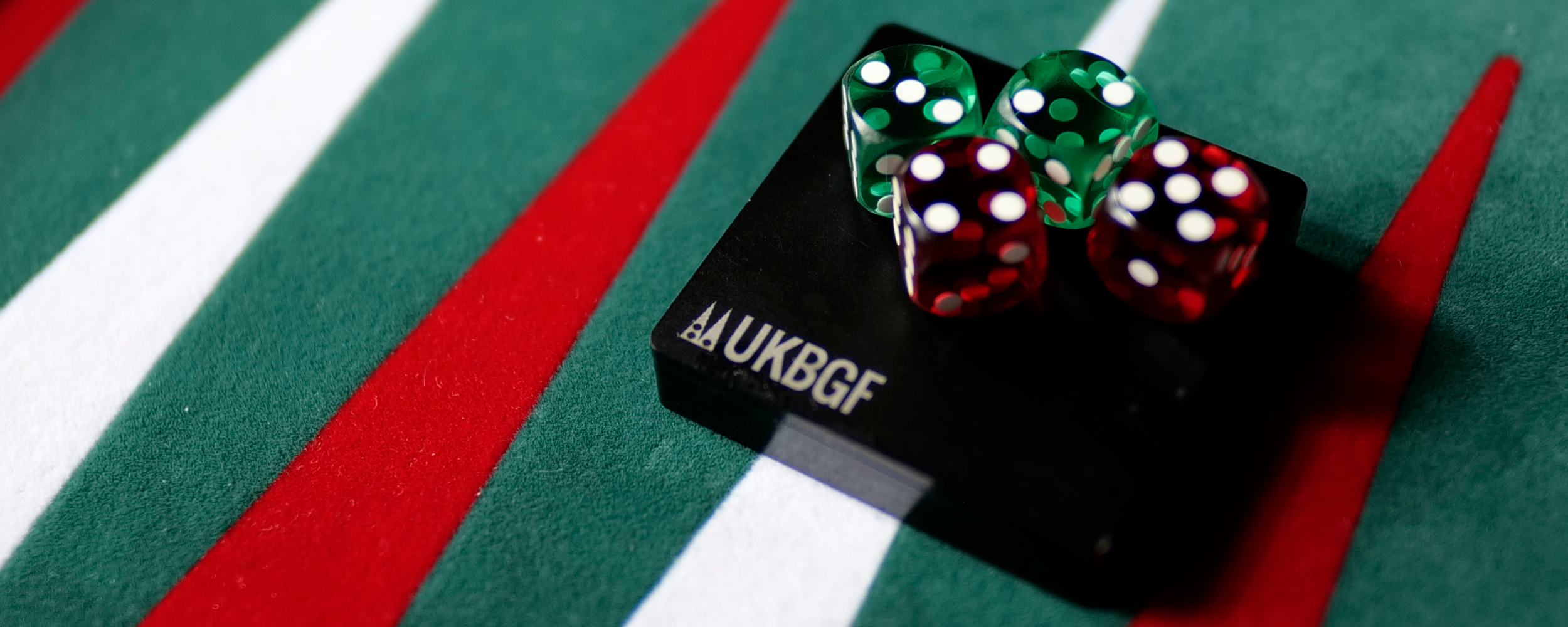 Close up of UKBGF branded precision red and green dice on green backgammon board.